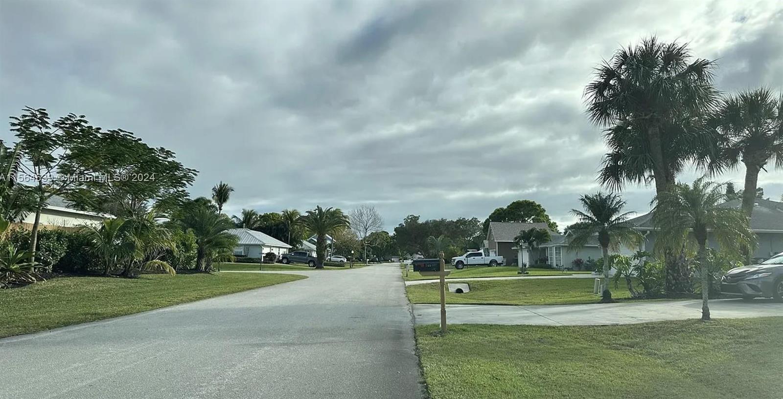A residential street features houses, palm trees, and parked vehicles under a cloudy sky — 755 38th Court, Vero Beach FL 32968, VERO BEACH, FL