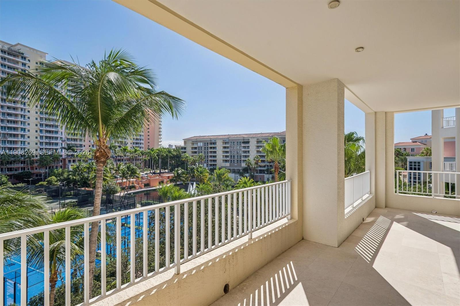 A covered balcony overlooks a tennis court, palm trees, and surrounding apartment buildings — 717 Crandon Blvd # 507, Key Biscayne FL 33149, KEY BISCAYNE, FL