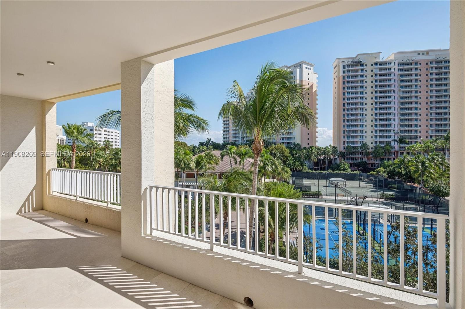 A balcony with white railings overlooks tennis courts, palm trees, and high-rise apartment buildings — 717 Crandon Blvd # 507, Key Biscayne FL 33149, KEY BISCAYNE, FL