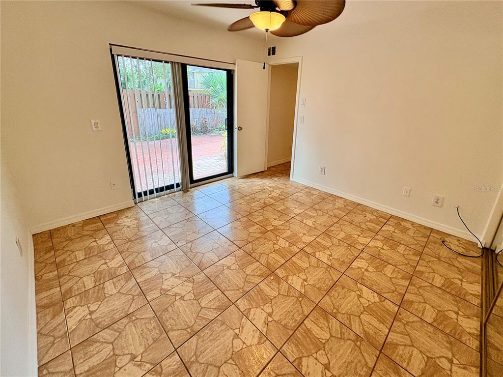 An empty room with tan tile flooring, a ceiling fan, and sliding glass patio doors — 18 CEDAR DUNES DRIVE, NEW SMYRNA BEACH, FL