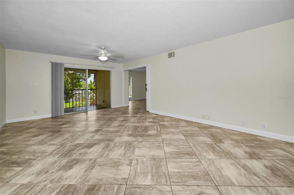 An empty living room features light-colored tile flooring, a ceiling fan, and a sliding glass door — 8765 BARDMOOR BOULEVARD UNIT 306, SEMINOLE, FL