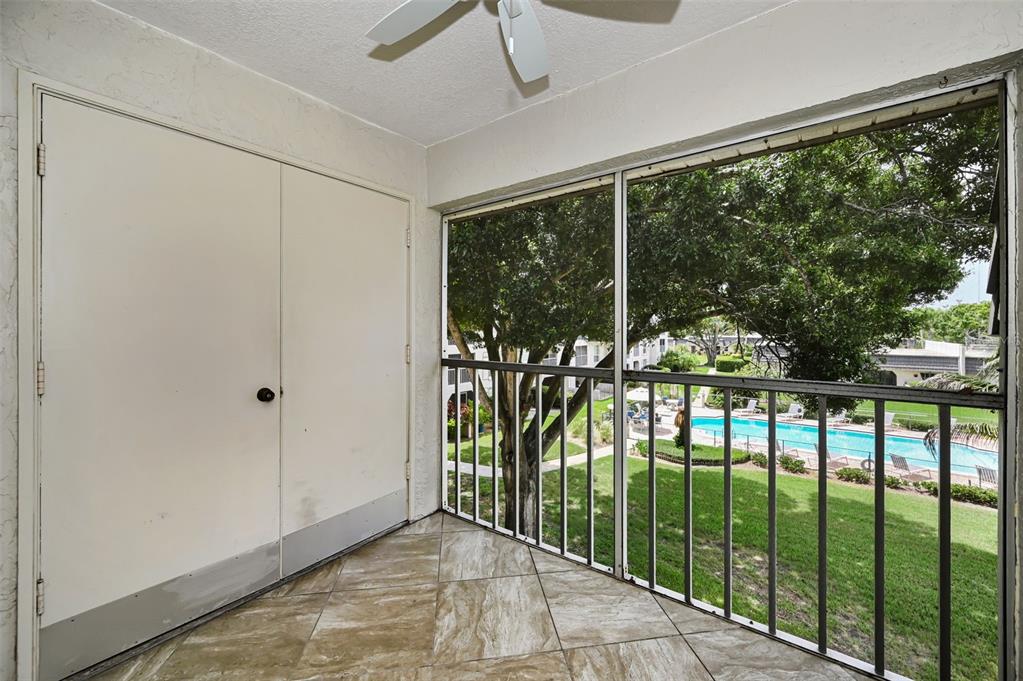 A screened-in balcony with tiled flooring overlooks a swimming pool and green space — 8765 BARDMOOR BOULEVARD UNIT 306, SEMINOLE, FL