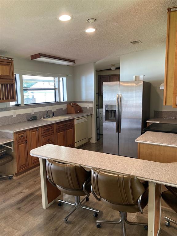 A kitchen features wood cabinets, a stainless steel refrigerator, and a breakfast bar with chairs — 1038 20TH STREET, OKEECHOBEE, FL