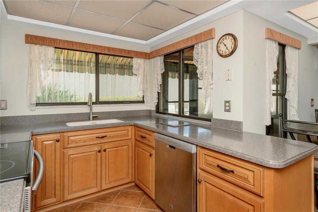 A kitchen with wood cabinets, gray countertops, a stainless steel dishwasher, and windows with curtains — 3825 GLEN OAKS MANOR DRIVE, SARASOTA, FL