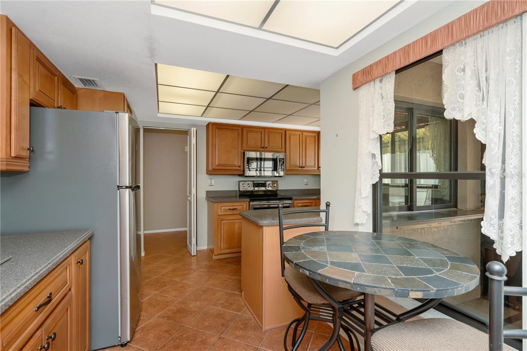 A kitchen with wood cabinets, stainless steel appliances, tile flooring, and a small dining table — 3825 GLEN OAKS MANOR DRIVE, SARASOTA, FL