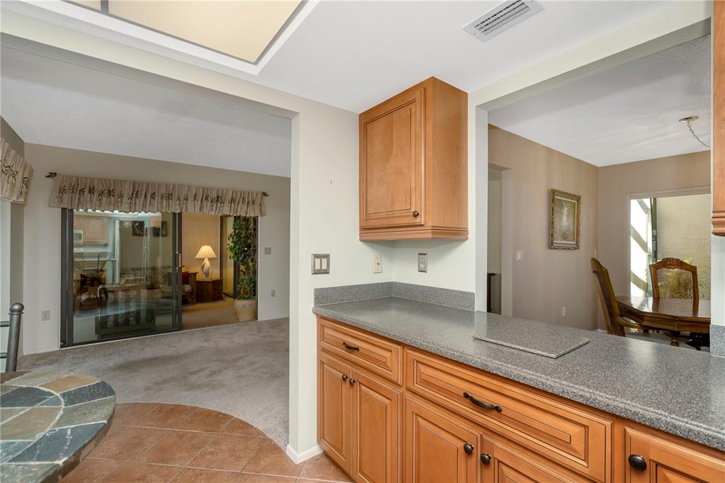 A kitchen counter with wood cabinets and gray countertops overlooks a carpeted living area — 3825 GLEN OAKS MANOR DRIVE, SARASOTA, FL