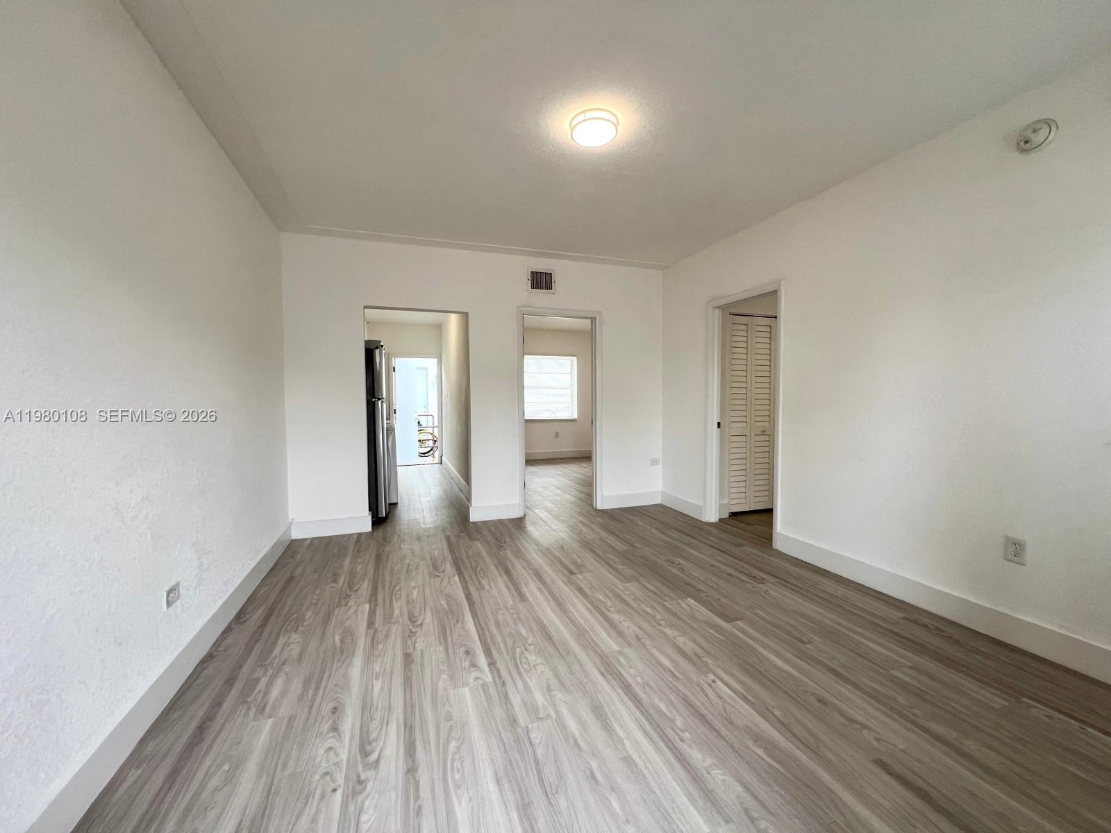An empty room features light wood-look flooring, white walls, and doorways leading to other spaces — 1900 Calais Dr # 1904, Miami Beach FL 33141, MIAMI BEACH, FL