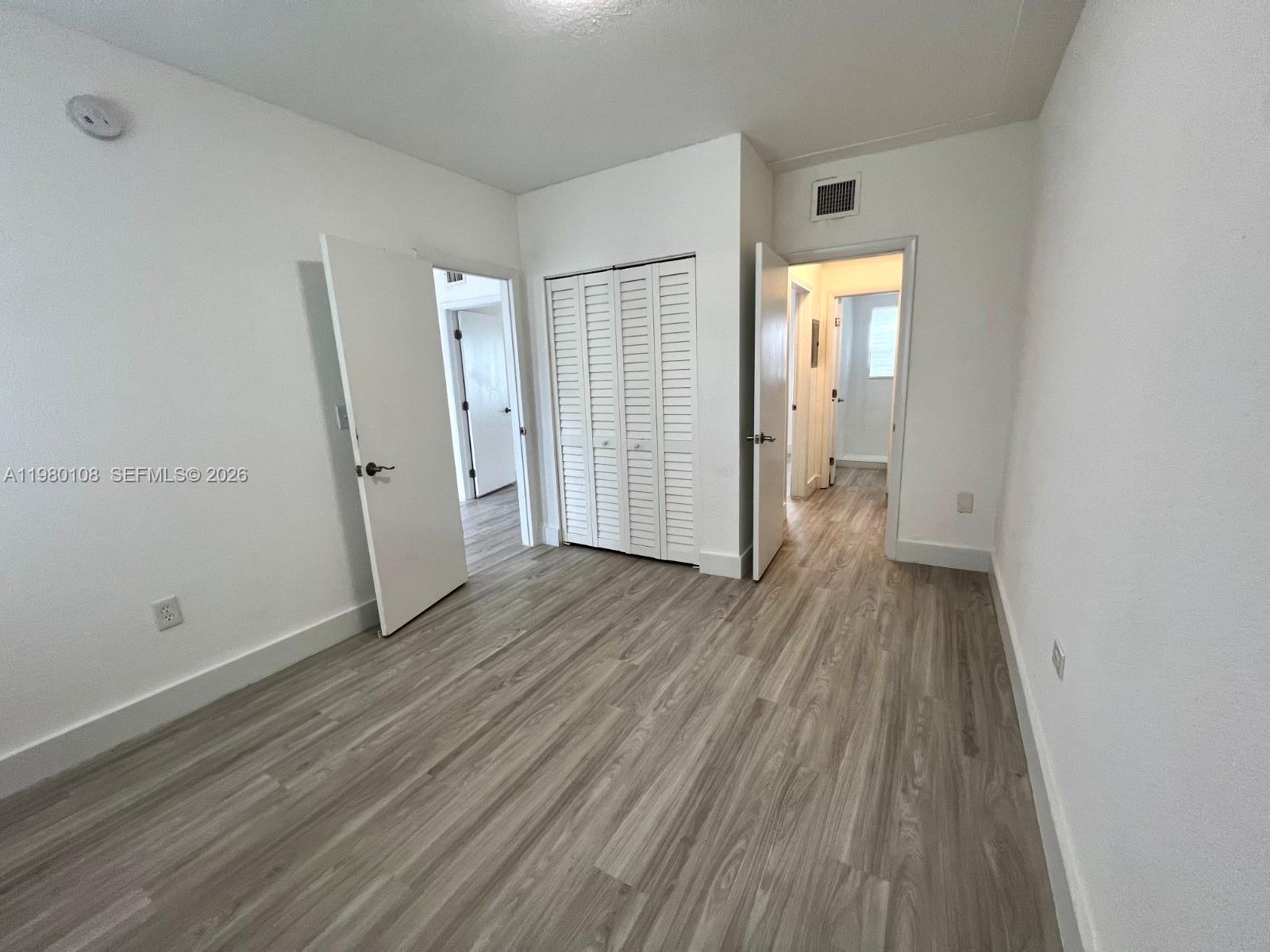 A bedroom with white walls, light wood-look flooring, and two open doorways — 1900 Calais Dr # 1904, Miami Beach FL 33141, MIAMI BEACH, FL