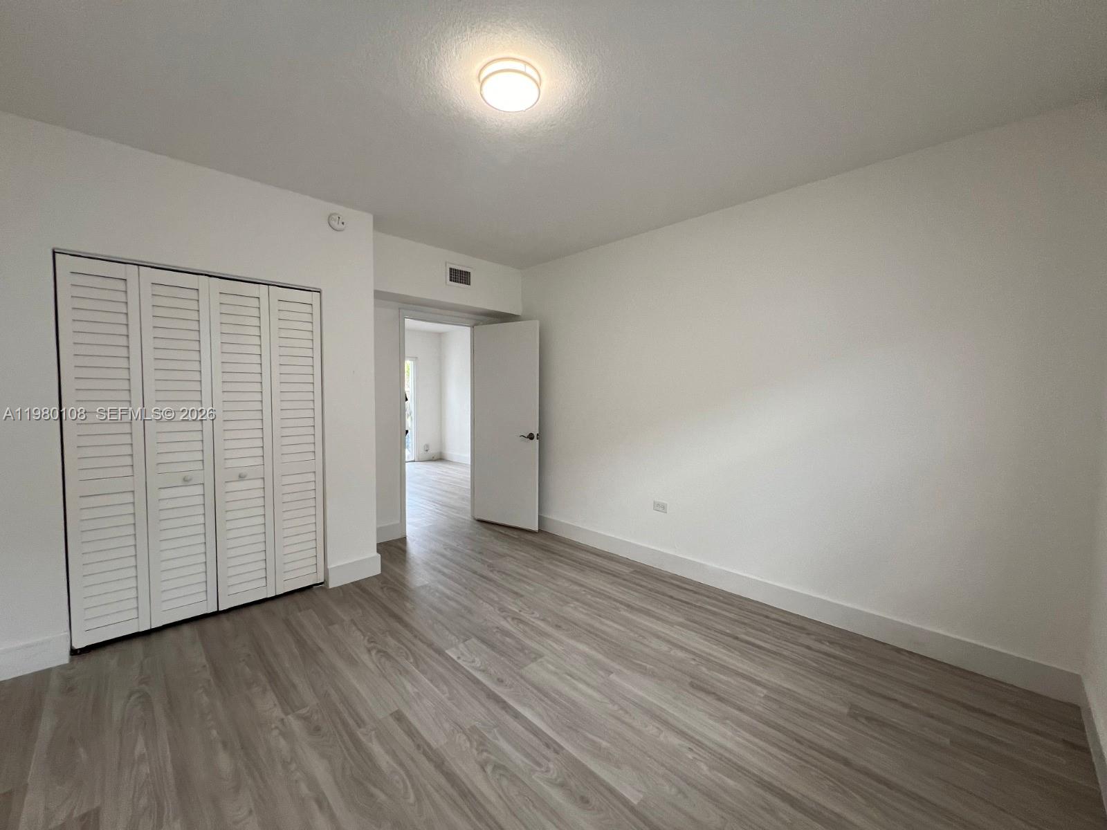 An empty room features white walls, light wood-look flooring, and a white louvered closet door — 1900 Calais Dr # 1904, Miami Beach FL 33141, MIAMI BEACH, FL