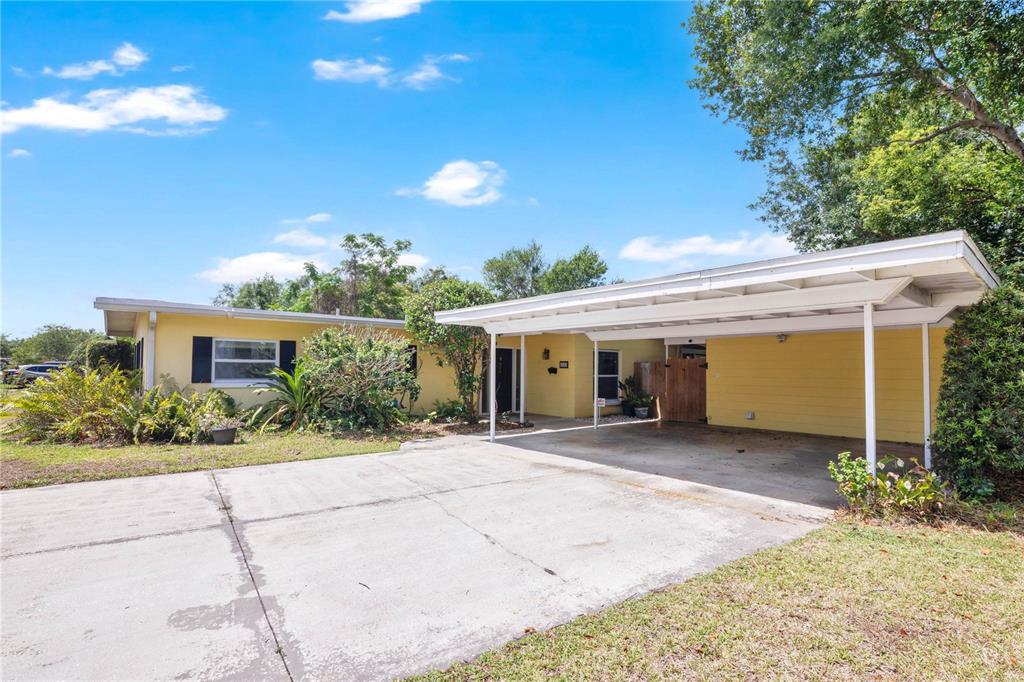 A yellow single-story house features a concrete driveway and a large attached white carport — 5020 SAINT MARIE AVENUE, BELLE ISLE, FL