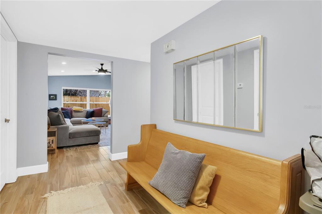 A hallway features light wood flooring, a wooden bench, and a large rectangular wall mirror — 5020 SAINT MARIE AVENUE, BELLE ISLE, FL