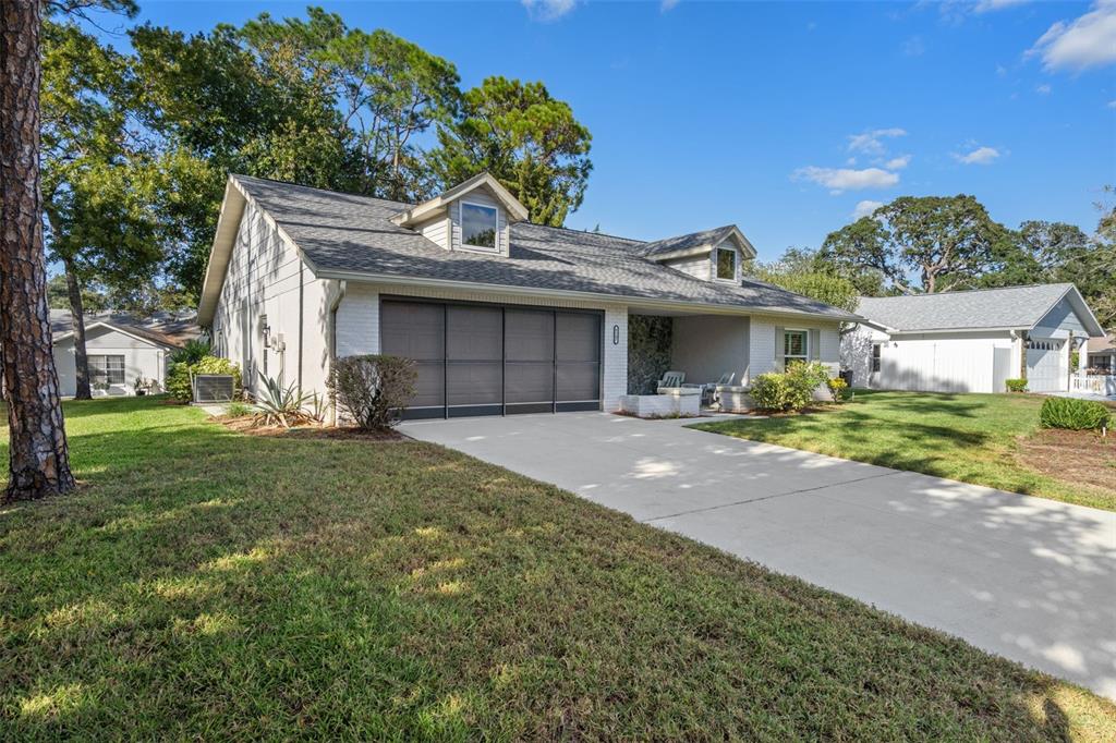 A single-story house with a white brick exterior, a screened garage, and two roof dormers — 6147 TURNBURRY COURT, SPRING HILL, FL