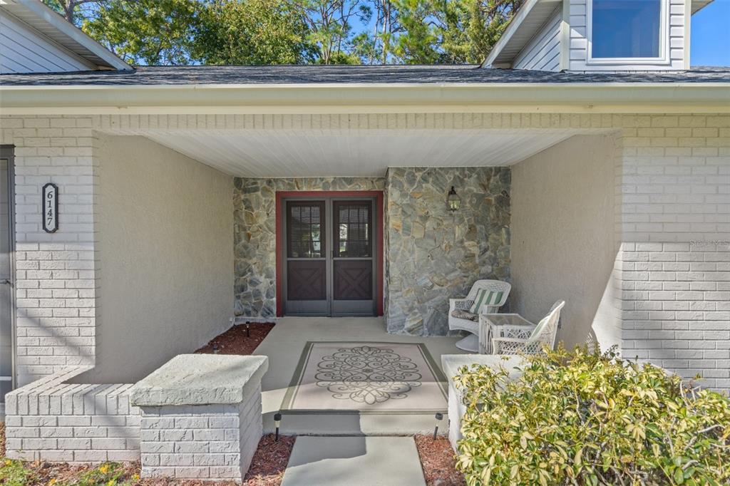 A covered front porch features a stone accent wall, double screen doors, and brick pillars — 6147 TURNBURRY COURT, SPRING HILL, FL