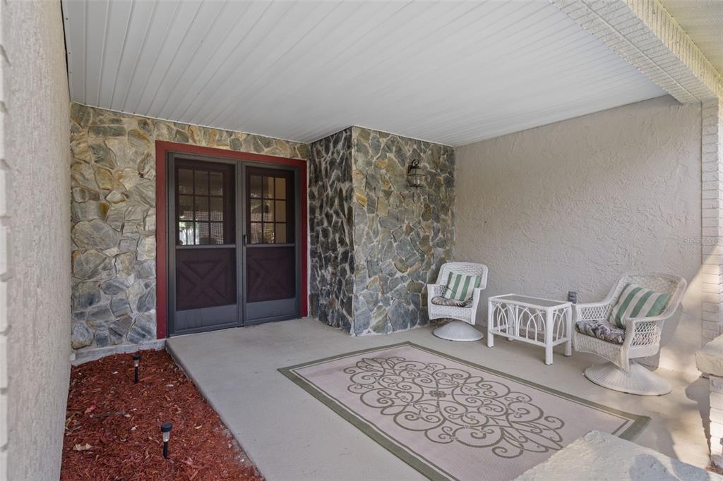 A covered porch features a stone accent wall, double screen doors, and two white wicker chairs — 6147 TURNBURRY COURT, SPRING HILL, FL