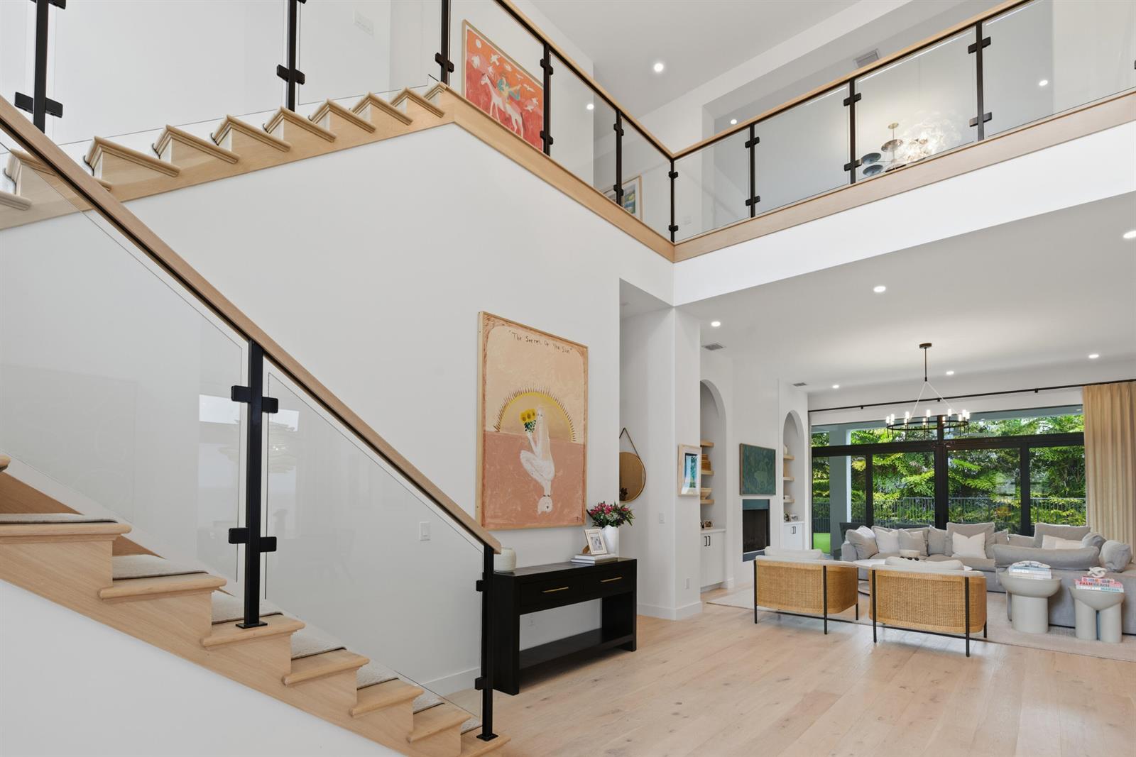 A bright, open-concept living area features a wooden staircase with glass railings and modern decor — 9593 Vescovato Way, Boca Raton FL 33323, BOCA RATON, FL