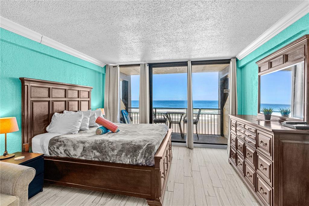 A bedroom with a wooden bed frame, teal walls, and a balcony overlooking the ocean — 2301 S ATLANTIC AVENUE UNIT 339, DAYTONA BEACH, FL