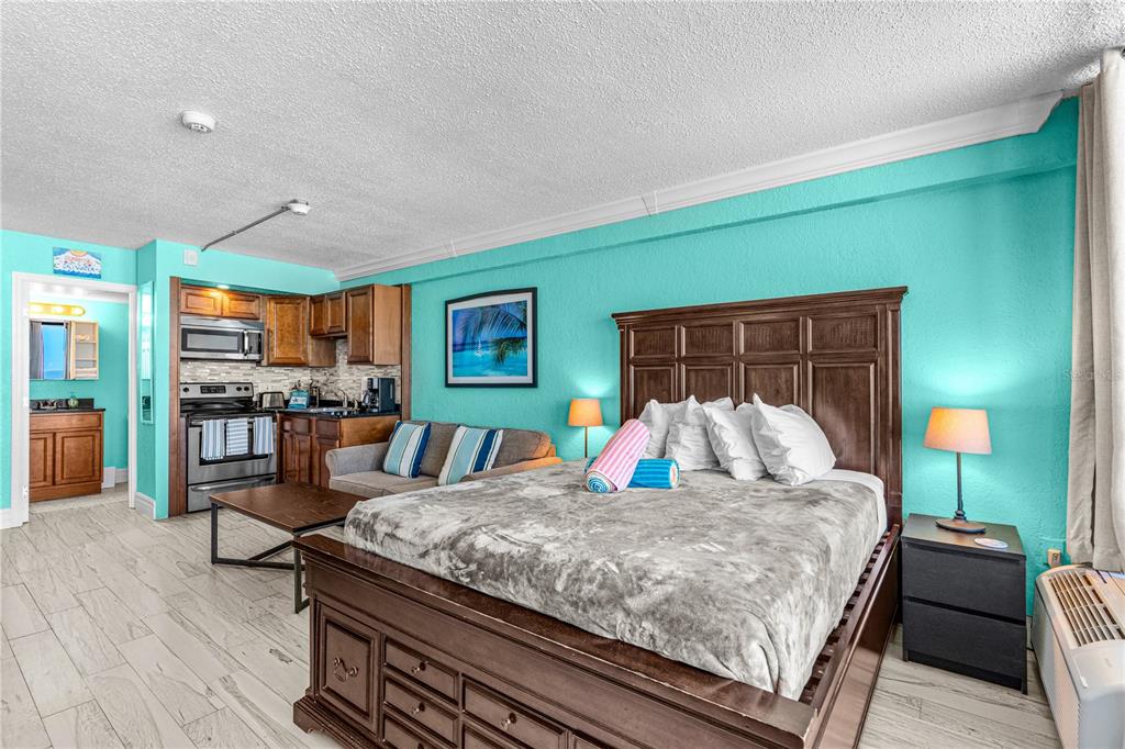 A studio hotel room features a bed, kitchenette, and turquoise walls with light wood flooring — 2301 S ATLANTIC AVENUE UNIT 339, DAYTONA BEACH, FL