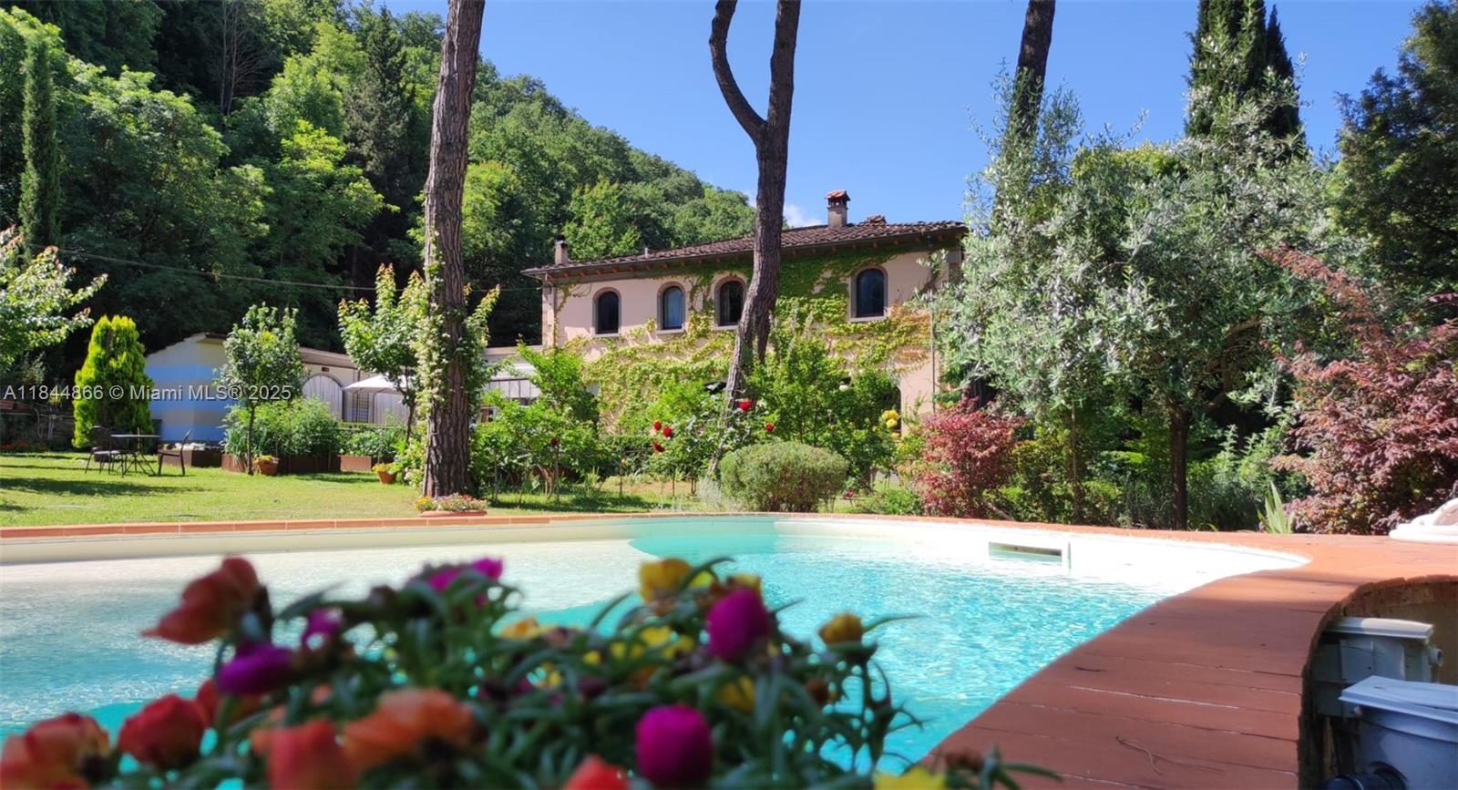 A swimming pool sits in the foreground of a garden with a two-story villa behind — 74 Castelnuovo - Subbiano, Tuscany, IA 52010, IA