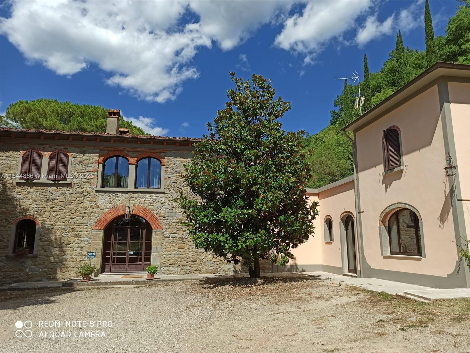 A stone building and a peach-colored structure flank a large tree in a courtyard — 74 Castelnuovo - Subbiano, Tuscany, IA 52010, IA