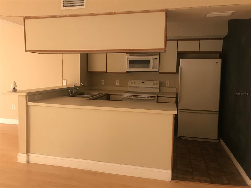 A kitchen with white appliances, light-colored cabinets, and a breakfast bar overlooking a living area — 2599 DOLLY BAY DRIVE UNIT 204, PALM HARBOR, FL