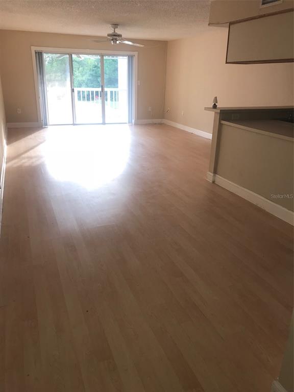 An open living area features light wood-look flooring, a ceiling fan, and sliding glass doors — 2599 DOLLY BAY DRIVE UNIT 204, PALM HARBOR, FL