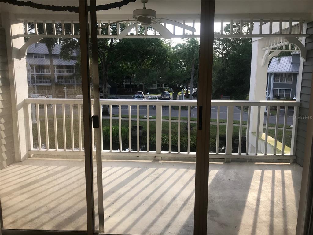 A covered balcony with a white railing overlooks a parking area and trees — 2599 DOLLY BAY DRIVE UNIT 204, PALM HARBOR, FL