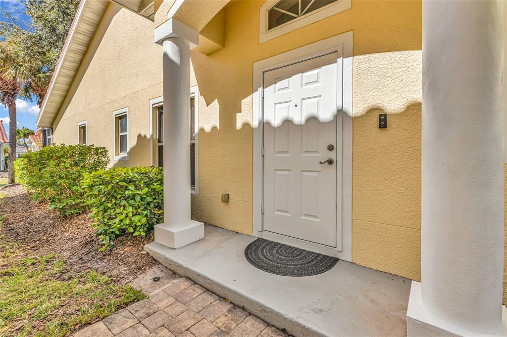 A yellow house exterior features a white front door, two columns, and a paved walkway — 3841 ALBACETE CIRCLE UNIT 51, PUNTA GORDA, FL