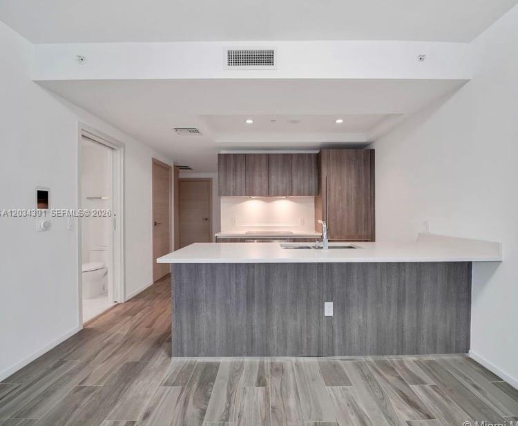 A modern kitchen features gray wood-grain cabinetry, a white island countertop, and light wood flooring — 801 S Miami Ave # 1807, Miami FL 33130, MIAMI, FL