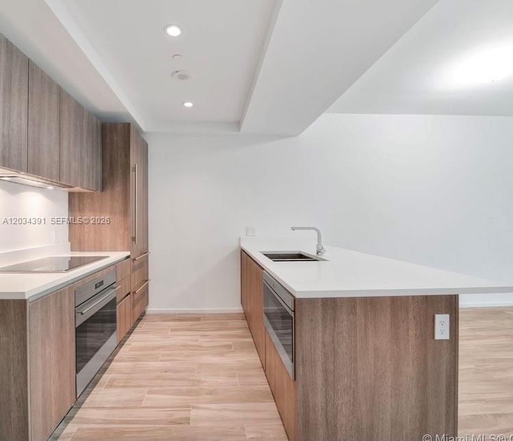 A modern kitchen features wood-grain cabinets, white countertops, stainless steel appliances, and light-colored flooring — 801 S Miami Ave # 1807, Miami FL 33130, MIAMI, FL