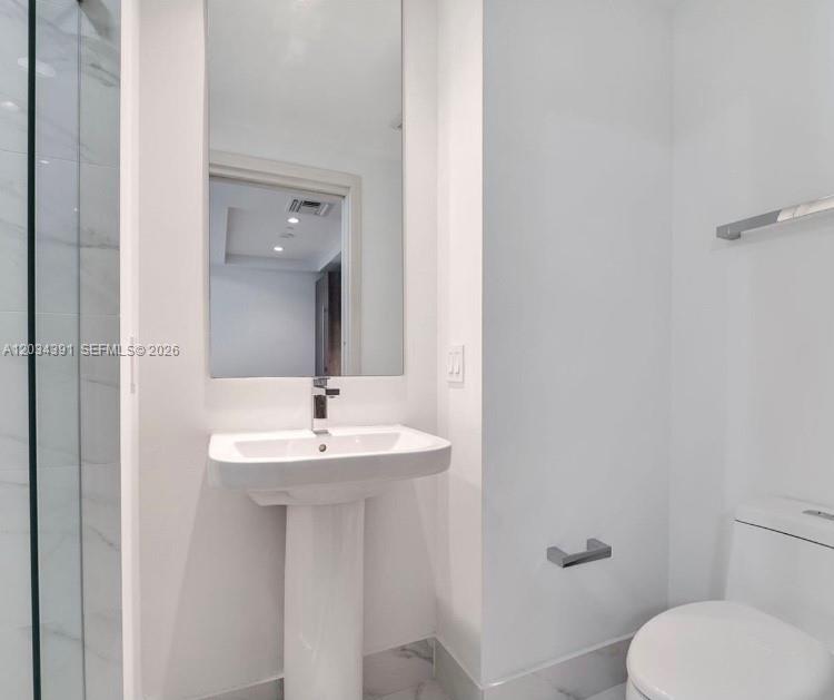 A modern bathroom features a pedestal sink, a wall-mounted mirror, and a glass-enclosed shower — 801 S Miami Ave # 1807, Miami FL 33130, MIAMI, FL