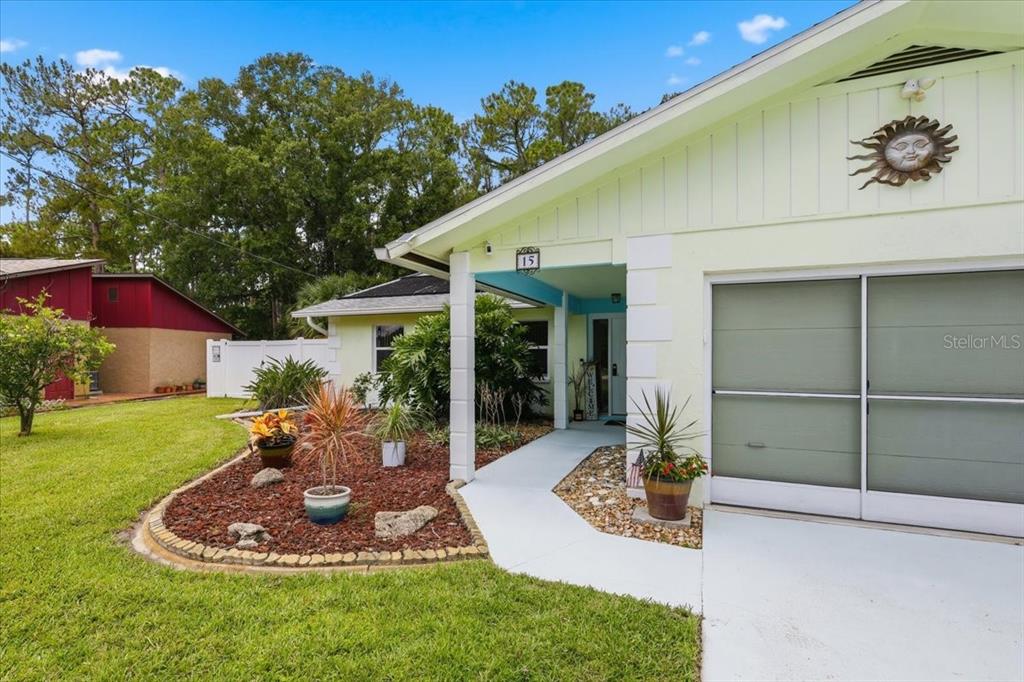 A light-colored house exterior features a covered entryway, a garage, and a landscaped front yard — 15 WASSERMAN DRIVE, PALM COAST, FL