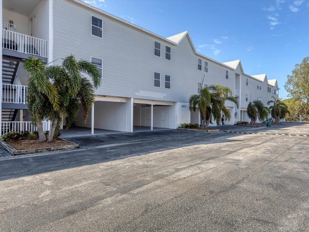 A multi-story apartment building with light gray siding and covered ground-level parking spaces — 3607 E BAY DRIVE UNIT 206, HOLMES BEACH, FL