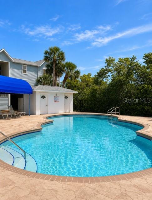 A swimming pool sits in front of a white building with a blue awning — 3607 E BAY DRIVE UNIT 206, HOLMES BEACH, FL