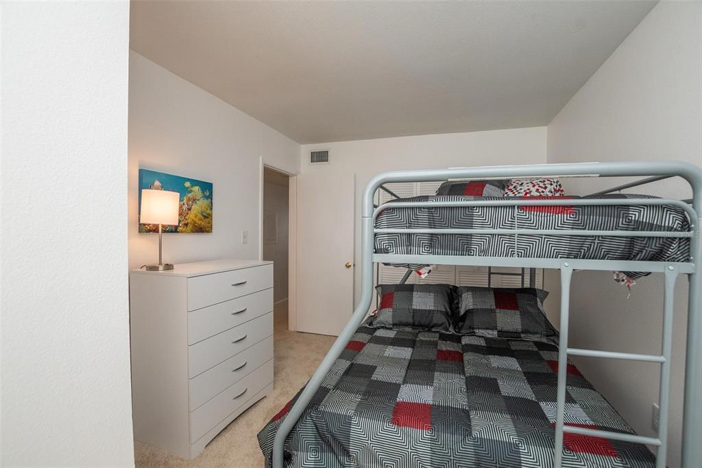 A bedroom features a metal bunk bed, a white dresser, and a lamp on carpet — 4849 SAXON DRIVE UNIT C202, NEW SMYRNA BEACH, FL