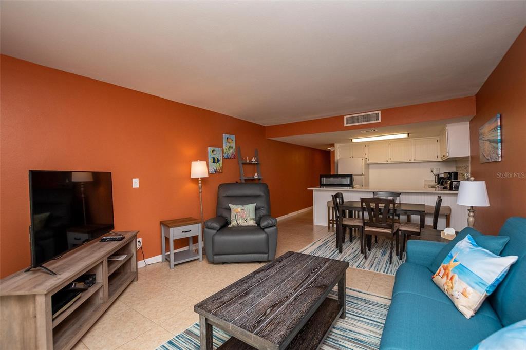 A living room with orange walls, tile floors, and an open kitchen with dining area — 4849 SAXON DRIVE UNIT C202, NEW SMYRNA BEACH, FL