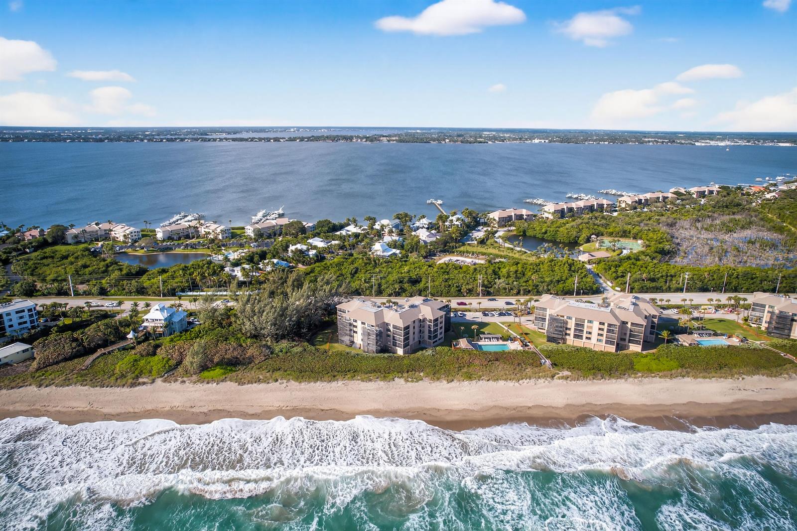 An aerial view shows beachfront condominiums, lush vegetation, and a large body of water — 2491 NE Ocean Boulevard # 106, Stuart FL 34996, STUART, FL