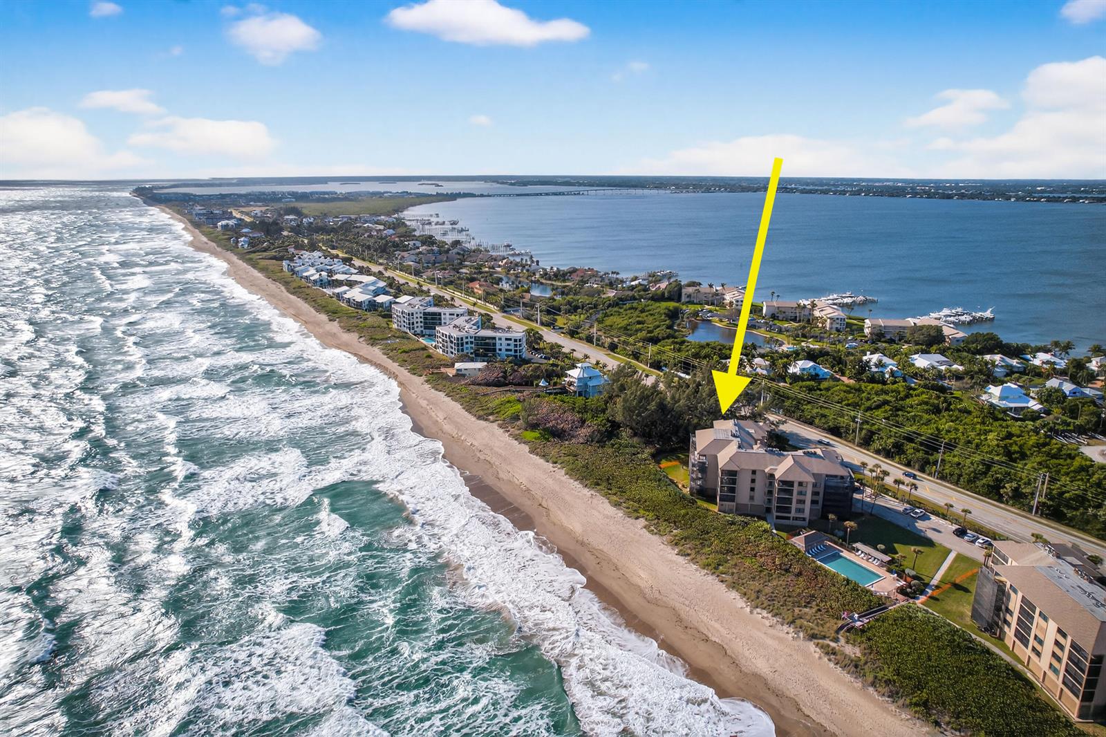 An aerial view shows a beachfront condominium building with a pool along the coast — 2491 NE Ocean Boulevard # 106, Stuart FL 34996, STUART, FL