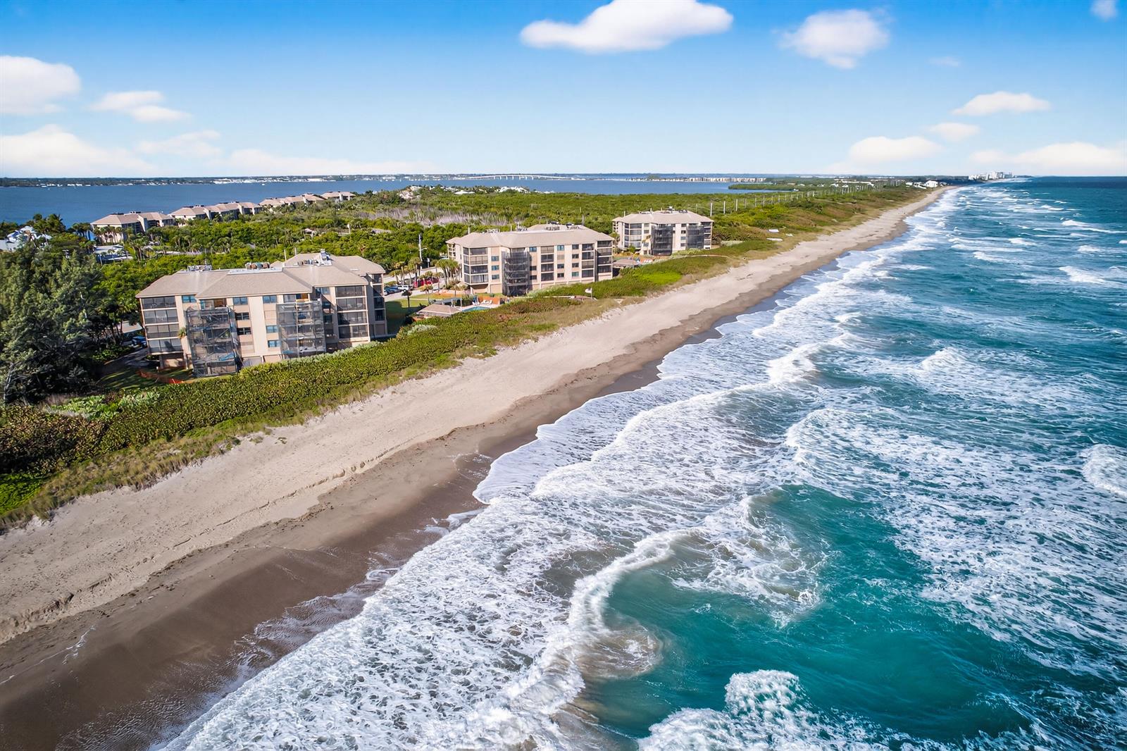 An aerial view of beachfront condominium buildings situated along a sandy coastline with ocean waves — 2491 NE Ocean Boulevard # 106, Stuart FL 34996, STUART, FL