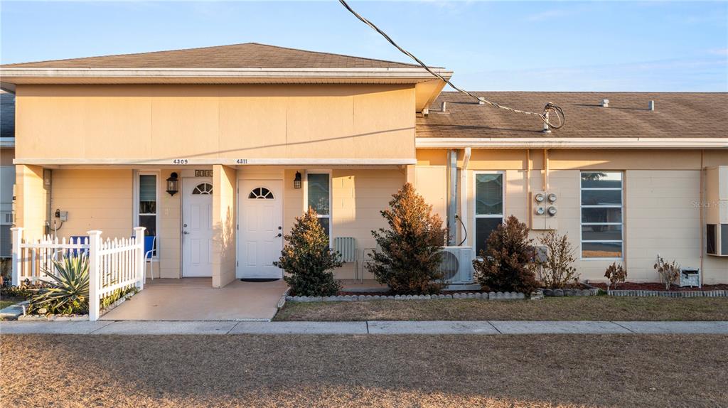The exterior of a single-story duplex features beige block walls, two white doors, and landscaping — 4311 CLUB CIRCLE, LAKESHORE, FL