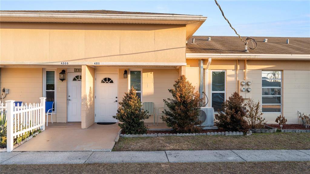 A single-story duplex with tan stucco walls, white doors, and a small front yard — 4311 CLUB CIRCLE, LAKESHORE, FL
