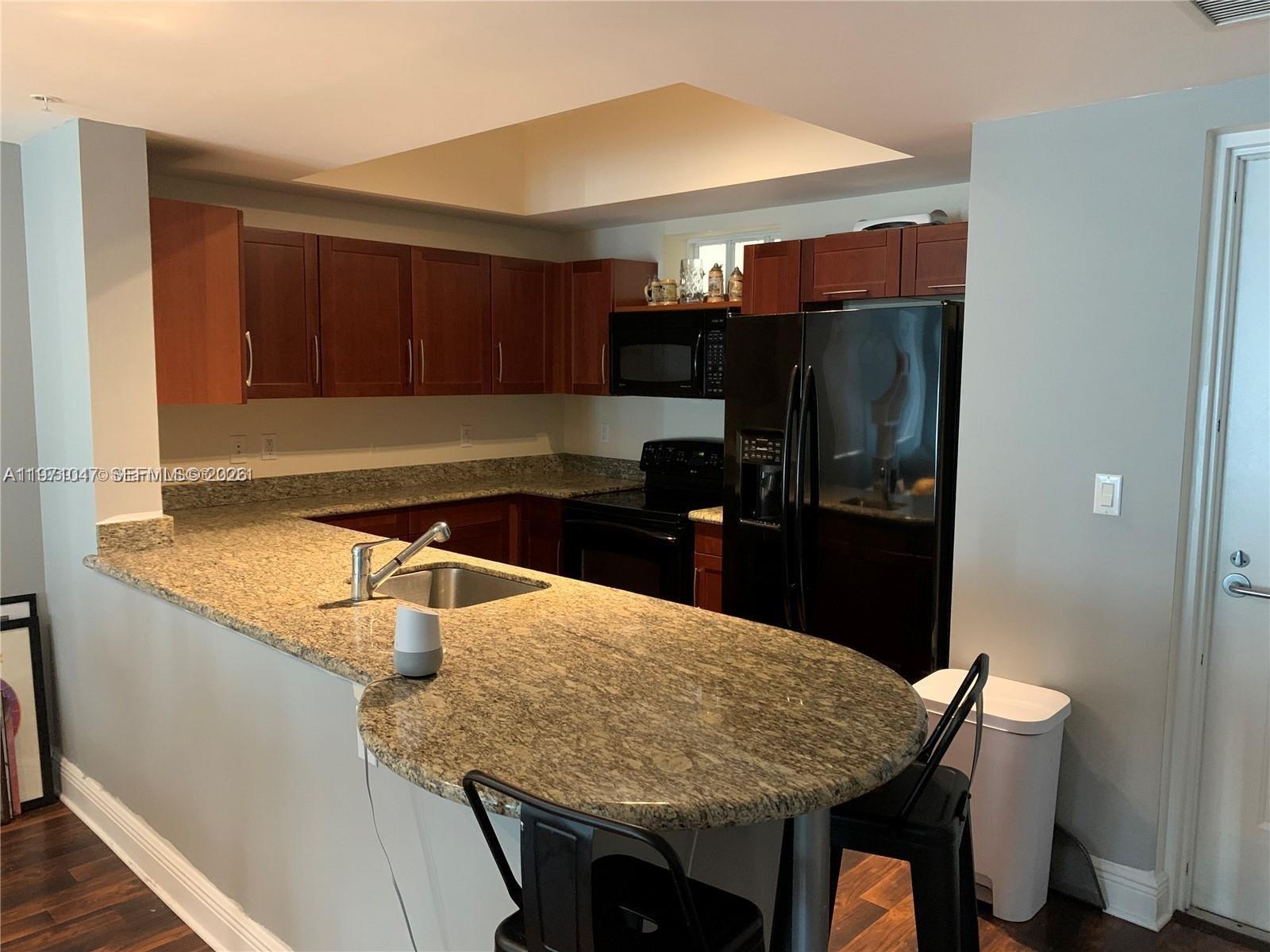 A kitchen features dark wood cabinets, granite countertops, black appliances, and a curved breakfast bar — 7275 SW 90th St # C312, Miami FL 33156, MIAMI, FL