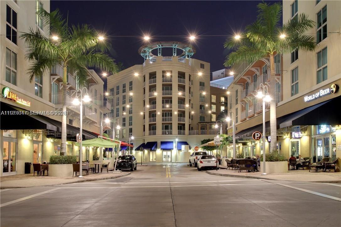 An exterior view of a street lined with buildings, palm trees, and storefronts at night — 7275 SW 90th St # C312, Miami FL 33156, MIAMI, FL