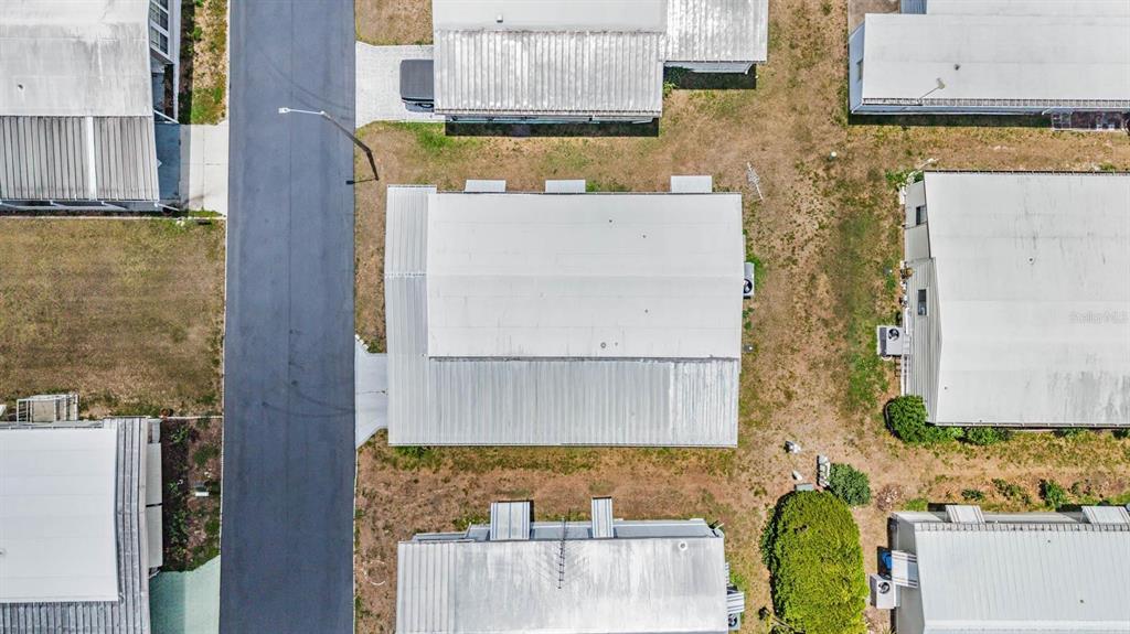 An aerial view shows a mobile home with a metal roof next to a paved road — 7203 EL MEYERS STREET, ZEPHYRHILLS, FL