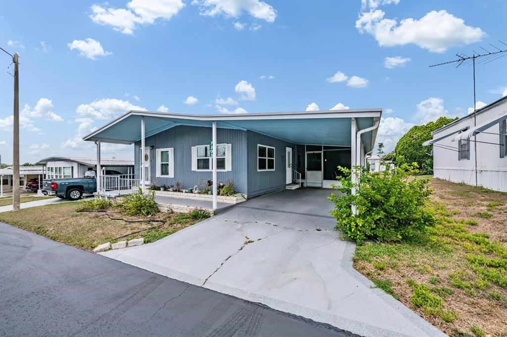 A blue manufactured home features a large attached carport and a concrete driveway — 7203 EL MEYERS STREET, ZEPHYRHILLS, FL