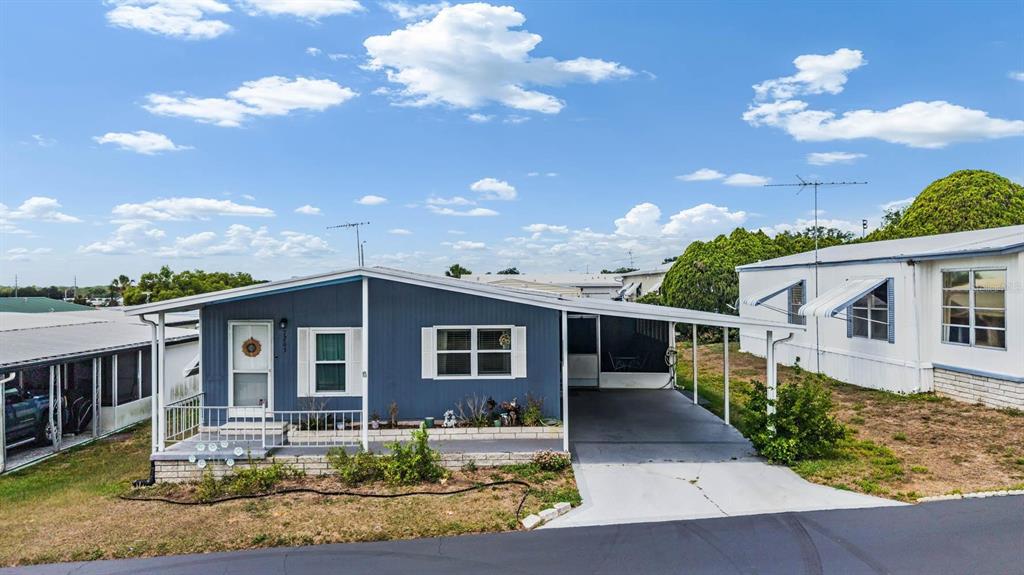 A blue manufactured home features a front porch, a carport, and a white-trimmed window — 7203 EL MEYERS STREET, ZEPHYRHILLS, FL
