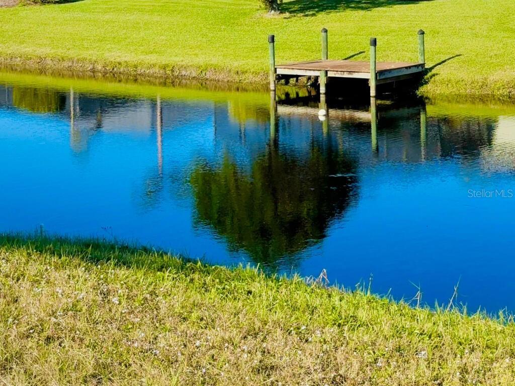 A wooden dock extends over a calm pond surrounded by green grass — 683 ROTONDA CIRCLE, ROTONDA WEST, FL