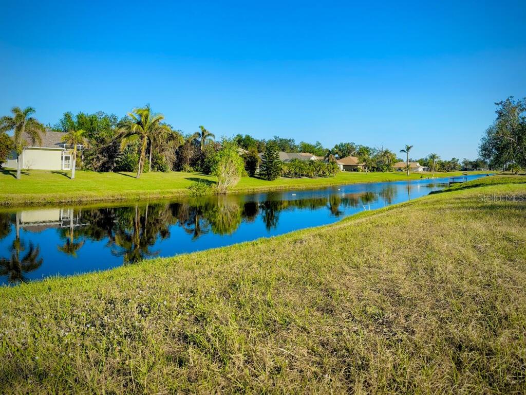 A grassy backyard slopes down to a calm canal lined with palm trees and houses — 683 ROTONDA CIRCLE, ROTONDA WEST, FL