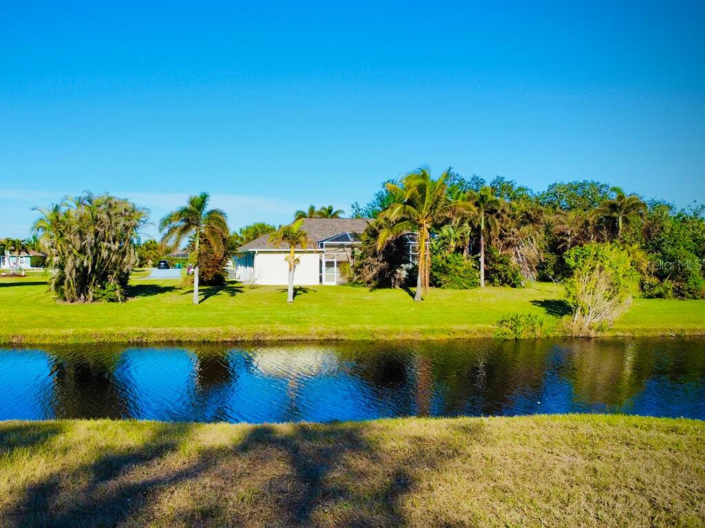 A single-story house with a screened lanai sits behind a canal and grassy lawn — 683 ROTONDA CIRCLE, ROTONDA WEST, FL