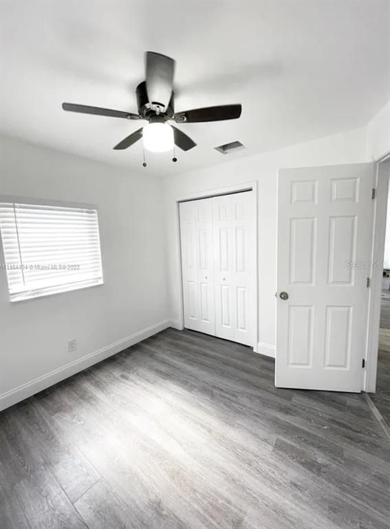 This bedroom features white walls, gray wood-look flooring, a ceiling fan, and a closet — 710 SW 9TH STREET, DELRAY BEACH, FL