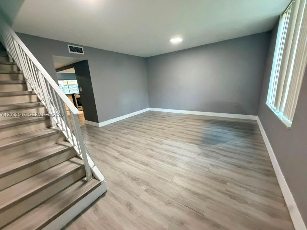An empty living room features gray walls, wood-look flooring, and a staircase with white railings — 274 NE 141st St # 3C, Miami FL 33161, MIAMI, FL